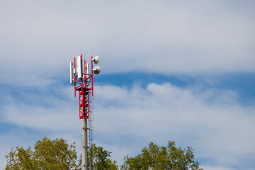 Radio tower for broadcasting signals of Internet and mobile communications installed in an inaccessible place against the background of the tops of green trees of red-white color from a metal frame.