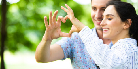 Romantic couple in love concept. Closeup of couple making heart shape with hands at park