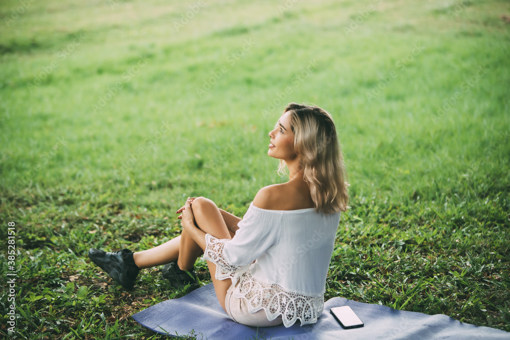 Wall mural cute caucasian girl relax and sitting at the green park outdoors in morning. cheerful beautiful woma