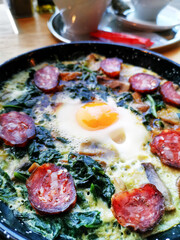 Omelet with spinach, mushrooms and chorizo cooked in old vintage pan served with three slices of bread on wooden plate.
