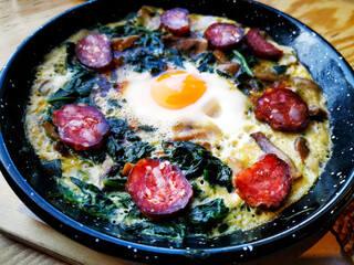 Omelet with spinach, mushrooms and chorizo cooked in old vintage pan served with three slices of bread on wooden plate.