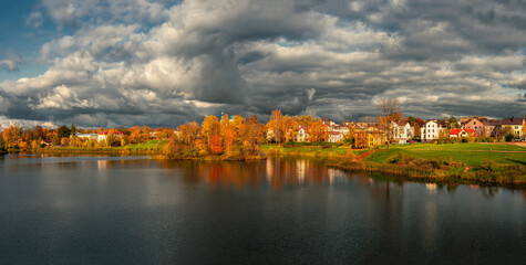 Fototapeta premium Wide panorama of the dramatic countryside with cottages and yellow trees on the lake shore.