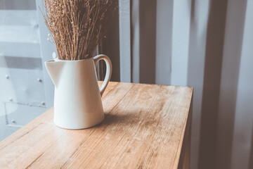 Selective focus and close up shot of cafe decorating with dried flowers in white ceramic jar on the wooden table near the glass window with snowflake decoration shows minimal style with copy space