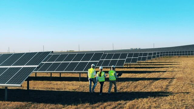 Safety inspectors are walking along the photovoltaic power field at a solar energy power plant.