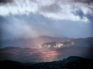 A single shaft of sunlight breaks through brooding storm clouds to illuminate the hillside of a...