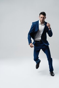 Full-length photo of funny man in suit running or jumping in air isolated over gray background