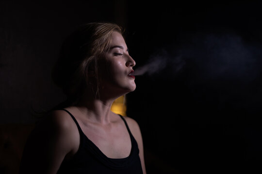 Beautiful girl with red lips blows smoke from a hookah from her mouth in cafe
