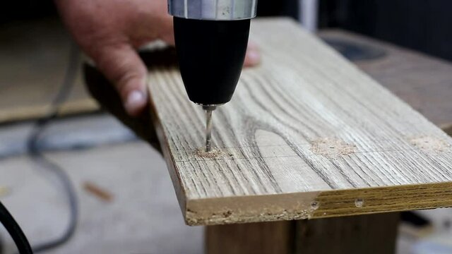 A man drills a hole in a wooden panel to make a country chair, close-up. Handmade, professional
