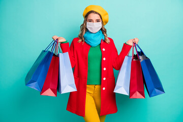 Photo of positive cheerful girl hold many bags wear mask red blue yellow sweater trousers isolated over turquoise color background