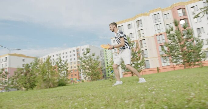 Young having fun with a disc on a summer meadow. Tracking shot of young men and woman throwing orange frisbee to each other in slow motion while having fun in park on summer day