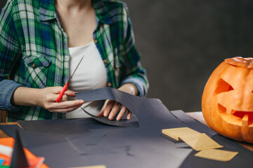 Closeup of a woman doing Halloween crafts. Detail of woman cutting paper with Jack-o-Lantern.