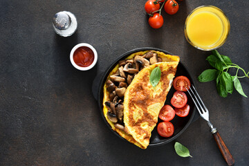 Omelet with mushrooms and tomatoes for breakfast with orange sticks on a concrete background.