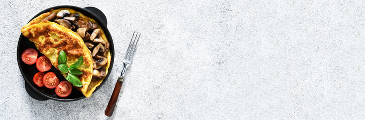 Omelet with mushrooms and tomatoes for breakfast with orange sticks on a white concrete background.