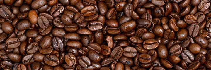 Full frame shot of roasted coffee beans for the banner. Panoramic background of fresh dark caffeine seeds on heap. A lots of brown aroma crop from close up panoramic.
