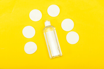 Makeup remove skin care. Tonic for face skin or makeup remover in a plastic bottle, cotton pads and wooden cotton buds on yellow background. Hygiene supplies, beauty tools and skin