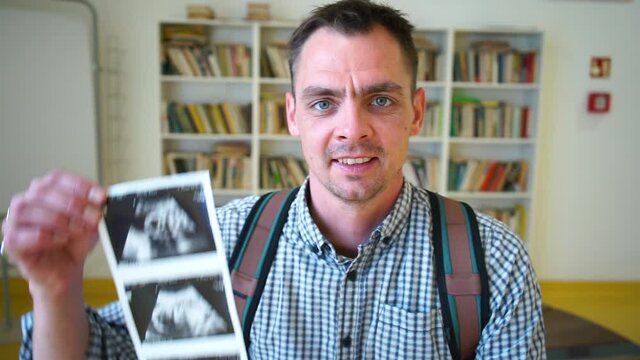 Portrait of a man showing a sonography image of a baby's fetus. The joy of a young parent, the news of his wife's pregnancy.