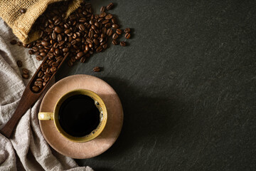 Close-up of Black hot coffee for morning with milk foam in old pink ceramic cup and napkin with coffee beans roasted in sack on dark table stone background. Top view, flat lay with copy space.