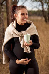 Beautiful young pregnant girl drinking tea in nature