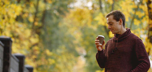 Man drinks a tea walking along fall alley