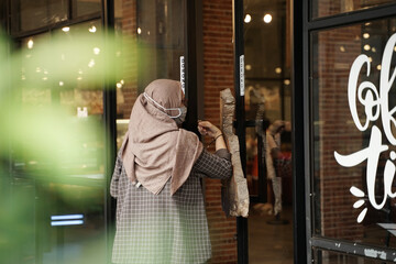 Muslim women are opening the glass doors of the cafe using their elbows in accordance with health...