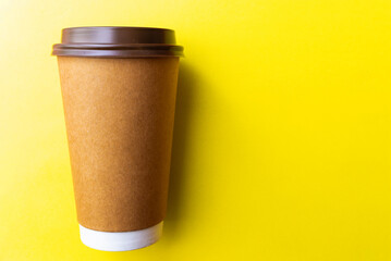 brown paper coffee cup on a yellow backgroud. Simple flat lay with copy space. Minimal concept.