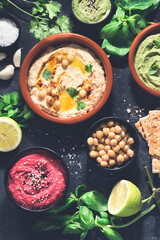 Flat lay of various types of vegetarian hummus based on herbs and beets, basil and coriander on a dark rustic background. Healthy vegetarian food concept, vegetable proteins
