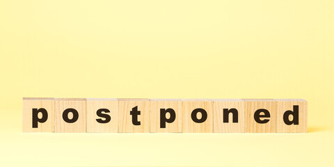 word postponed with small wooden blocks on yellow background