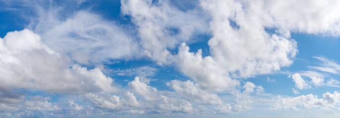 Fluffy cumulus clouds, translucent cirrus and stratus clouds float slowly across the bright blue sky on a sunny day. Panoramic skyscape shot. Weather, meteorology and types of clouds. - obrazy, fototapety, plakaty