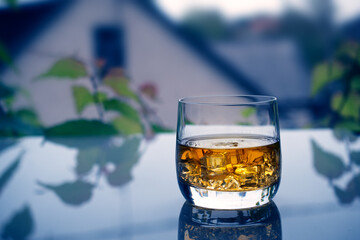A glass of whiskey with ice on an transparent table in the evening.
