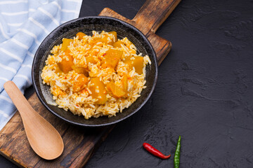 Rice with pumpkin curry in a black ceramic bowl, placed on a black table, top view.
