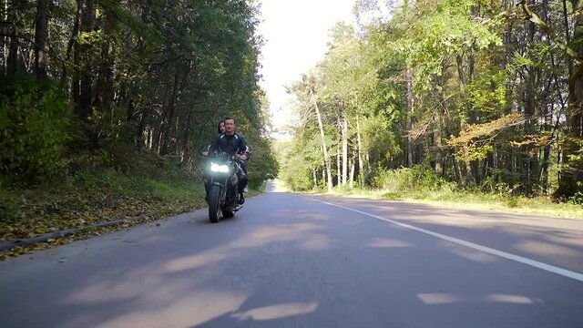 young happy couple in love motorcyclists in black leather jackets on a sports bike ride on the road smiling and hugging. Young sexy woman with boyfriend drive. Lifestyle. through the woods and trees