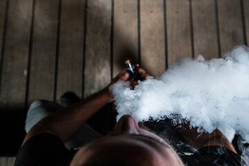 Young man sit and exhale smoke from his electronic cigarette, seen from above