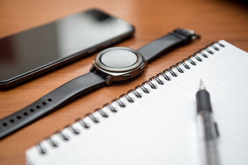 Notebook, smartphone and smartwatch with black screen on wooden table.