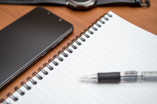 Notebook, smartphone and smartwatch with black screen on wooden table.