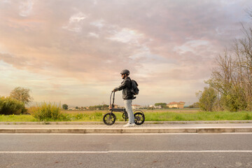 Smiling man with helmet and his electric bicycle at sunset. Commuter and new transportation...