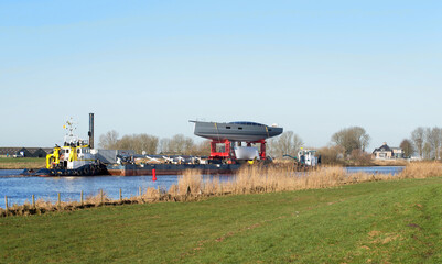 Fototapeta na wymiar Transport of a super sailing yacht on pontoon with towing boats. River. Zwartewater. Genemuiden