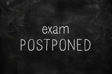 Exam postponed written with white and red chalk on blackboard