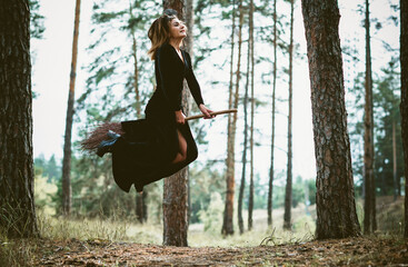 Young beautiful and mysterious Witch woman Flying on the Broom in woods. Levitation, a witch on a...