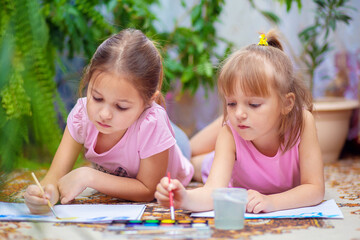 Two girls paint with paints lying on the floor at home or in kindergarten. Home leisure