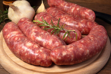 Salsiccia di maiale fresca disposta su un tagliere di legno con rosmarino e aglio.