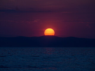 Sun setting behind a mountain by the coast