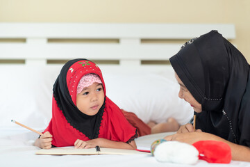 Young muslim girl writing a book with grandma, islamic child do homework at home