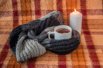 Obraz na płótnie Canvas old checkered blanket with orange red and brown patterns. autumn background. lit candle. cozy woolly gray scarf. cup of coffee