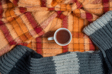 old checkered blanket with orange red and brown patterns. autumn background. cozy woolly gray scarf. cup of coffee
