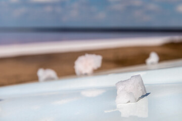Pink white salt flake crystal formation on white reflective surface with blurred pink salty lake landscape background. Spa resort sunny close-up
