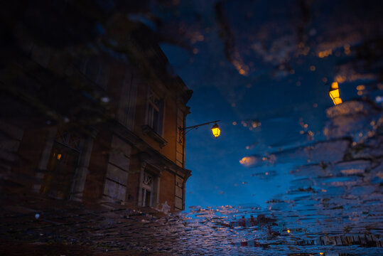 old street lamp reflected in the puddle. rainy day. cobble stone street. night photo