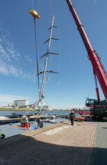Placing a mast at a super sailing yacht at the harbor. Hoisting. Lifting a mast of a ship with a crane. Shipbuilding industry.
