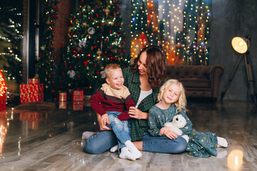 Cute mother with daughter and son posing at the Christmas tree