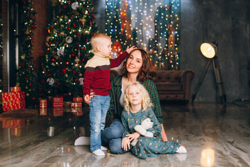 Cute mother with daughter and son posing at the Christmas tree