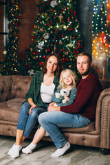Cute family mom, dad and daughter pose at the Christmas tree